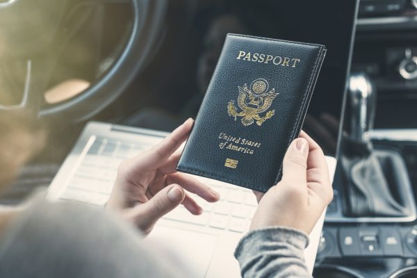 Woman in the car with laptop and american passport. Travel concept.